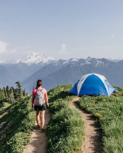 A backpacker walks towards her tent with a view of Mount Rainier in the background