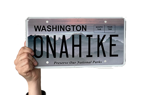 Hand holding license plate reading "ON A HIKE"