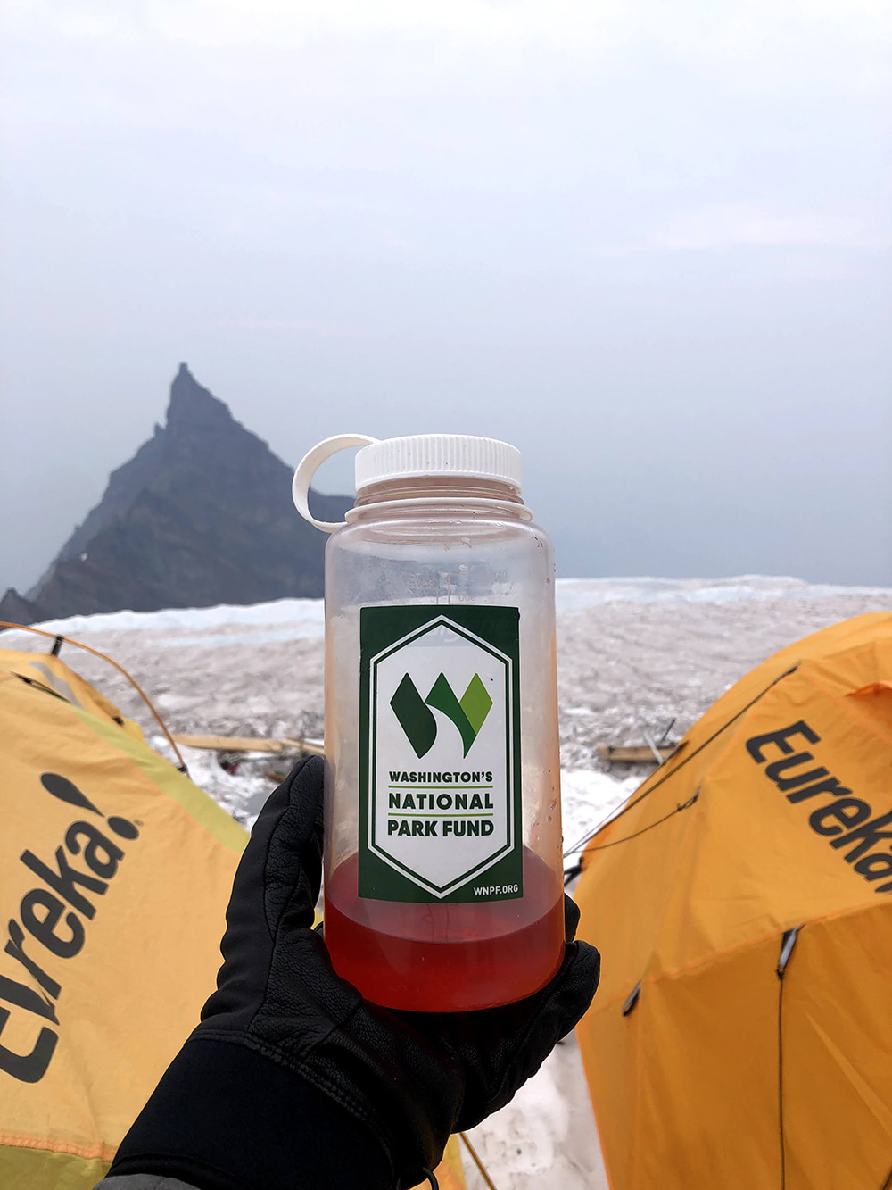 A water bottle with a WNPF sticker is held in front of a mountain