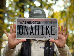 A woman holds a license plate in front of trees