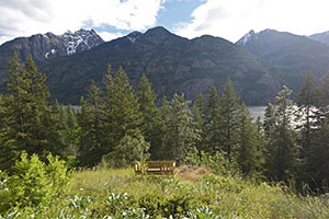 A bench with a view of trees, a lake, and mountains behind it