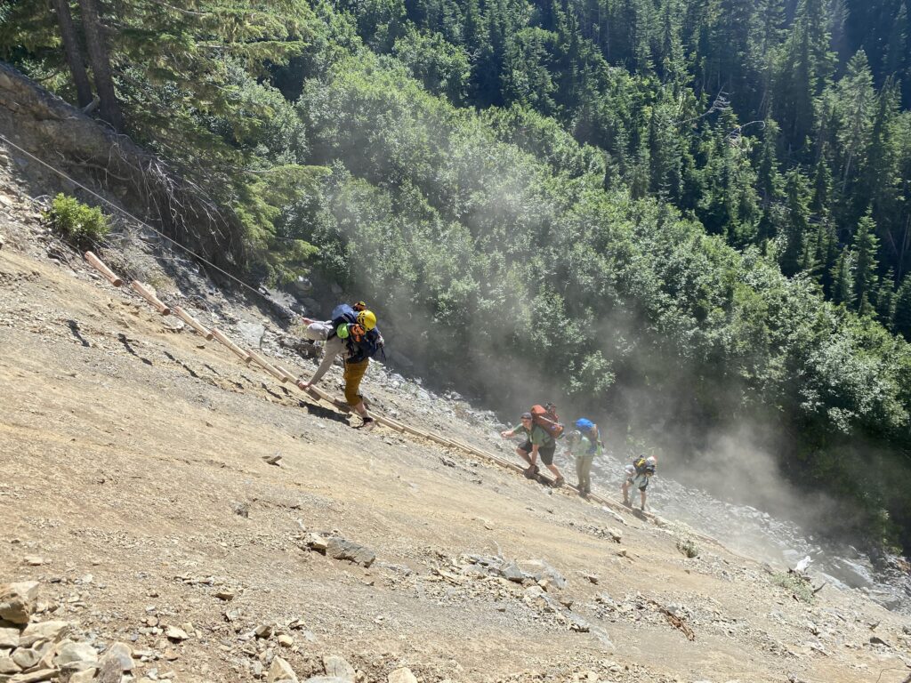 Four climbers with backpacks descending a ladder on a steep hill.