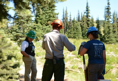 Three volunteers wearing hard hats while doing trail work.