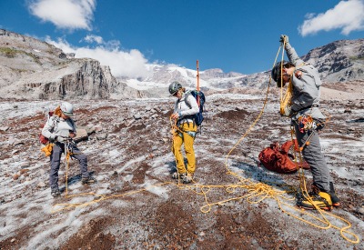 Three scientists holding a rope connecting them together to travel safely on the glacier.