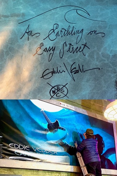 Image of Eddie Vedder signing a large blue poster that reads "An Earthling on Easy Street"