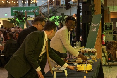 Three men grabbing desserts off a table.