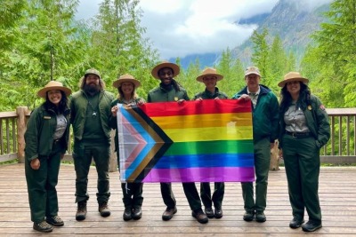 Seven park rangers stand on a boardwalk holding a pride flag.