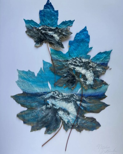 an image of mountains and glaciers painted on three maple leaves. hues of blue and white.