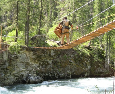 A man crosing a suspension bridge hanging above a river.