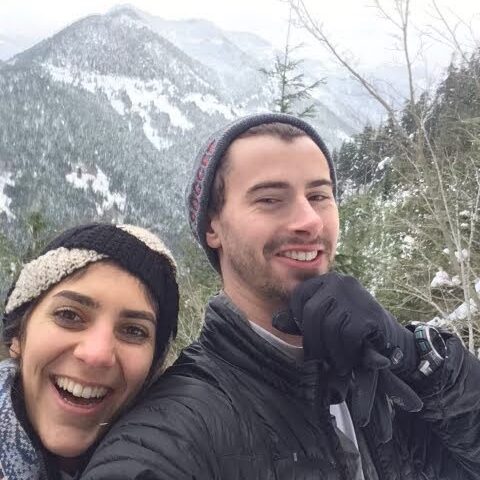 Woman on the left and man on the right smiling in front of a snowy mountain.