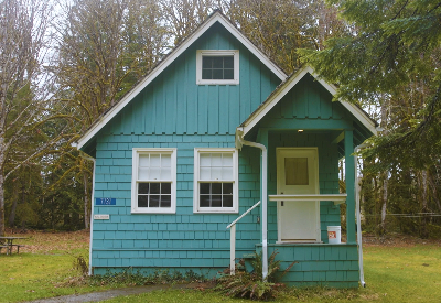 Small blue house with three windows and a door surrounded by trees.