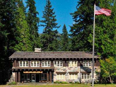 A wooden building nestled between trees with an American flag to the right of the building.