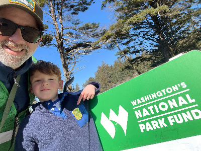 Photo of a father and son next to a green sign that reads "Washington's National Park Fund"