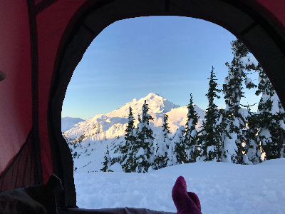 A photo taken fom inside a red tent with the door open to a snowy view of Mount Baker