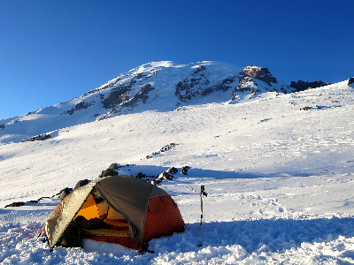 an orange tent on a snow field with a mountain in the background.