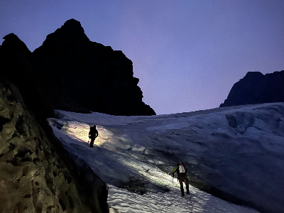A silhouette of two people wearing headlamps on a glacier.