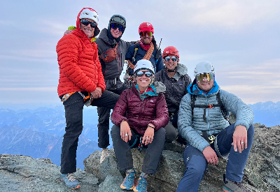 6 people standing on rocks smiling, wearing helmets and warm clothing.