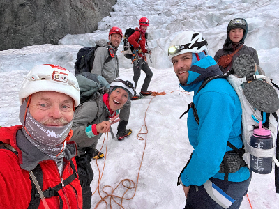 6 people wearing climbing gear standing and smiling on a glacier