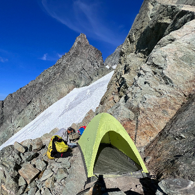 A green tent pitched on rocks with a glacier in the background