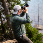 A man sitting on a rock looking through the viewfinder of his camera