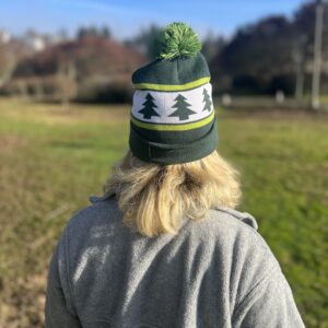A woman turned away from the camera, wearing a green and white beanie with three trees in the design.