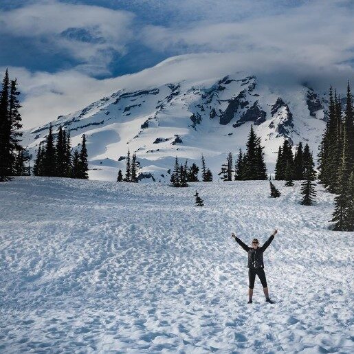 a person standing in a snow field with their hands up and the mountain behind them.