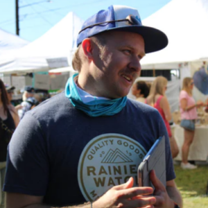 A man wearing a blue hat and tshirt that reads "Rainier Watch"