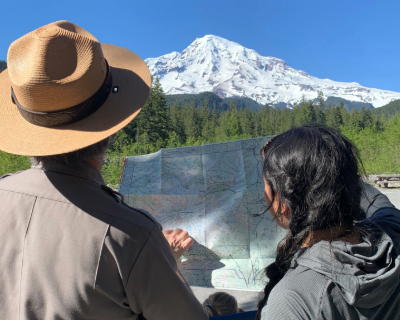 Photo of a ranger and a woman looking at a map with Mount Rainier in the back