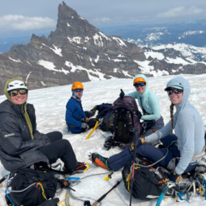 A groupd of four climbers sitting on a snowy glacier with Little Tahoma peak in the back.