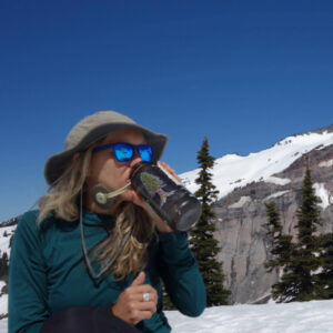 A woman drinking from her water bottle with a mountain in the background.