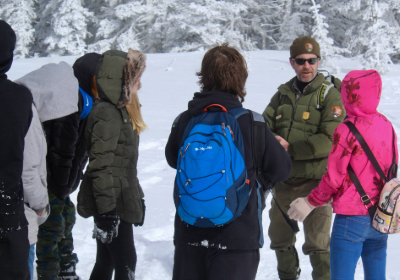 A group of students gathering around a park ranger while standing in the snow.