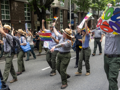 A group of park rangers in flat hats walking in a pride parade