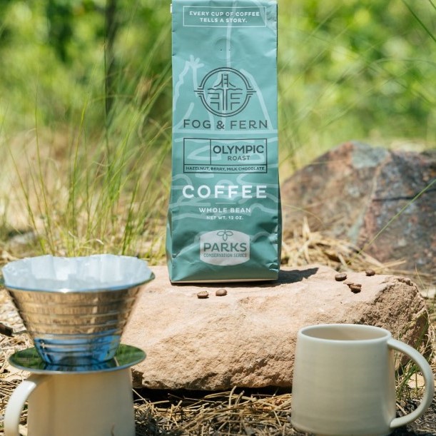 A blue coffee bag sitting on a rock and two coffee mugs on the ground