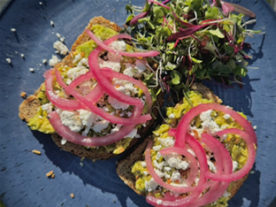 Two slices of avocado toast with feta and pickled red onions to top. 