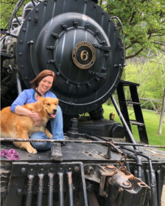 A woman and a dog sitting at the front of a train with teh number six on it.