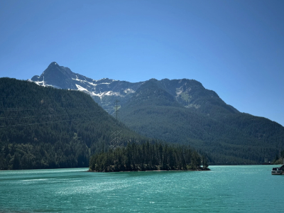 A turquoise blue lake with a small island of trees and a mountain in the back with blue skies.