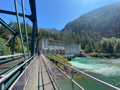 A view of a powerhouse building and a turquoise river rushing under a bridge.