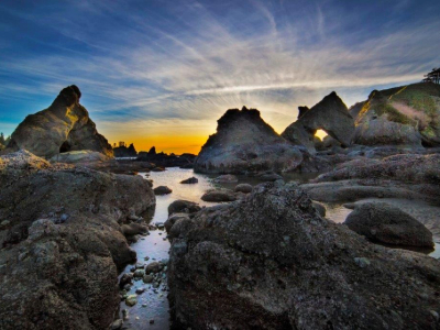 A sunset image of large rocks and tidepools on a beach.