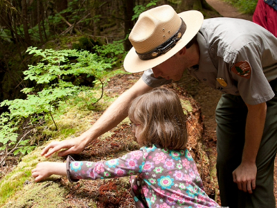 a park ranger with a young child observing vegetation outdoors.