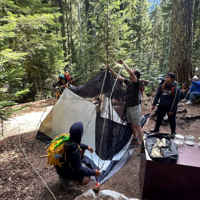 A group of three teenages setting up a black and white tent in a campground.