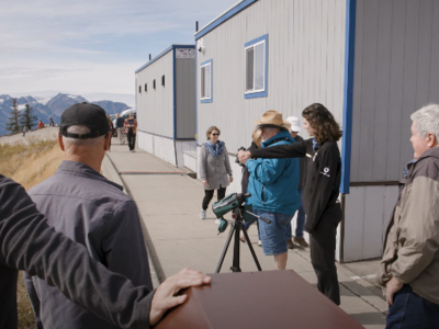 A group of 6 people standing by a telescope, looking at nearby wildlife in a field.